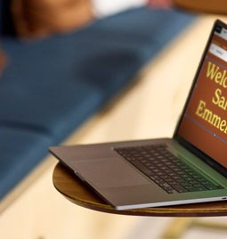 Open laptop on a wooden table displaying 'Welcome to Salon Emmeline' Squarespace template on screen with a blurred sofa in the background.