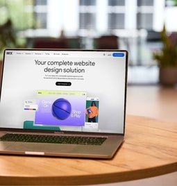 Laptop on a wooden table in a modern office environment, displaying the Wix website builder on-screen