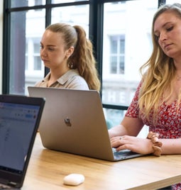 Two focused women working on laptops in a bright office environment