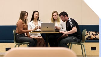 A group of four colleagues collaborating on a project with a laptop in an office environment.