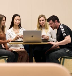 A group of four colleagues collaborating on a project with a laptop in an office environment.