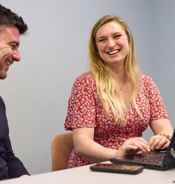 Two colleagues laughing and enjoying a productive meeting in the office with laptops on the desk.