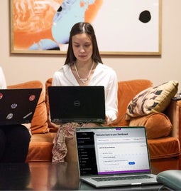 Two individuals working on laptops in a cozy co-working space, with a third laptop on the desk facing an empty chair, showing a Wix dashboard.