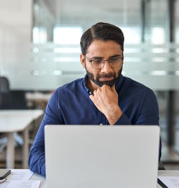 Man working at a desk looking at a laptop screen in an office