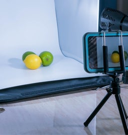 cell phone on a tripod taking a professional picture of two limes and a lemon in front of a white background