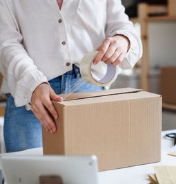 Photo of a woman packing up a parcel box with tape