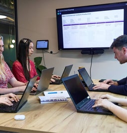 A group of professionals collaborating at a business meeting with laptops and presentation screen.