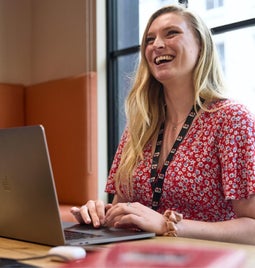 A joyful professional woman smiling while working on her laptop at an office desk.