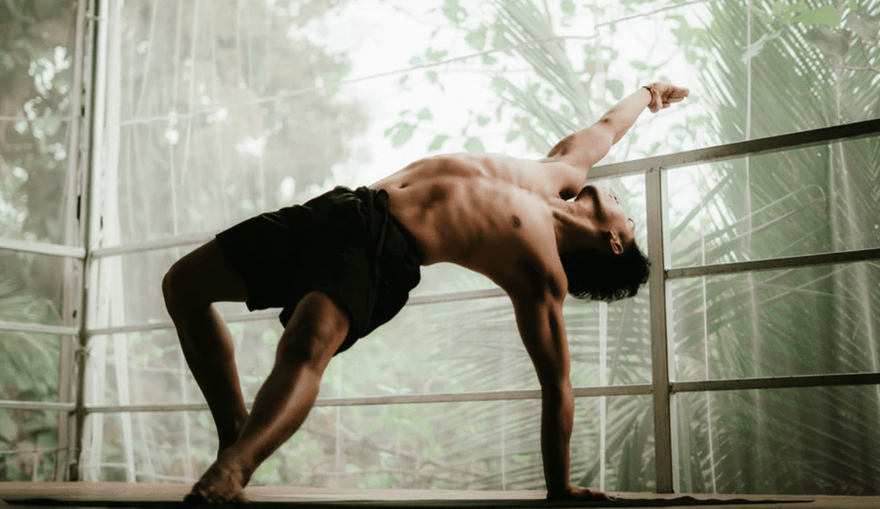 A man stretching into a yoga pose surrounded by nature.