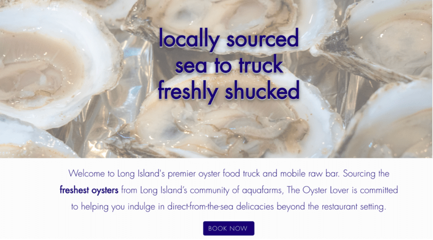 A close-up photo of a plate of oysters on a wooden table. The oysters are arranged in a spiral pattern, and they are surrounded by lemon wedges and cocktail sauce. The plate is sitting on a white tablecloth, and there is a fork and spoon on the side.