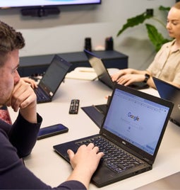 Man looks thoughtfully at the Google search on his laptop screen, as part of a business meeting with colleagues in an office.