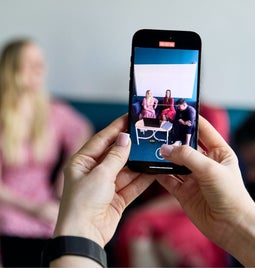 Person using a smartphone to photograph friends sitting across the table.