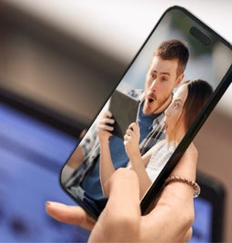 Hand holding smartphone, with an image of a comically surprised-looking couple on the screen.