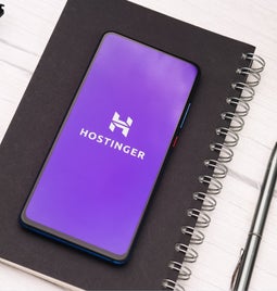 Phone showing Hostinger logo resting on a black notebook