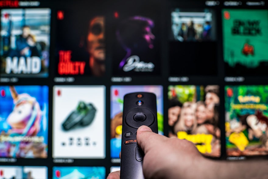 Blurred image of Netflix's content with a hand holding a TV remote pointing at the screen