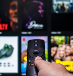 Blurred image of Netflix's content with a hand holding a TV remote pointing at the screen