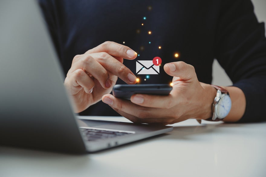 Person holding a mobile phone with a symbol for a new email floating above the device