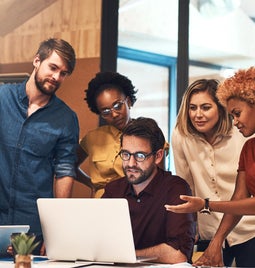 A group of six people standing/sitting around a laptop