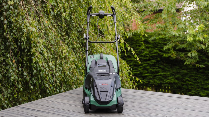 A green lawn mower positioned on a wooden deck