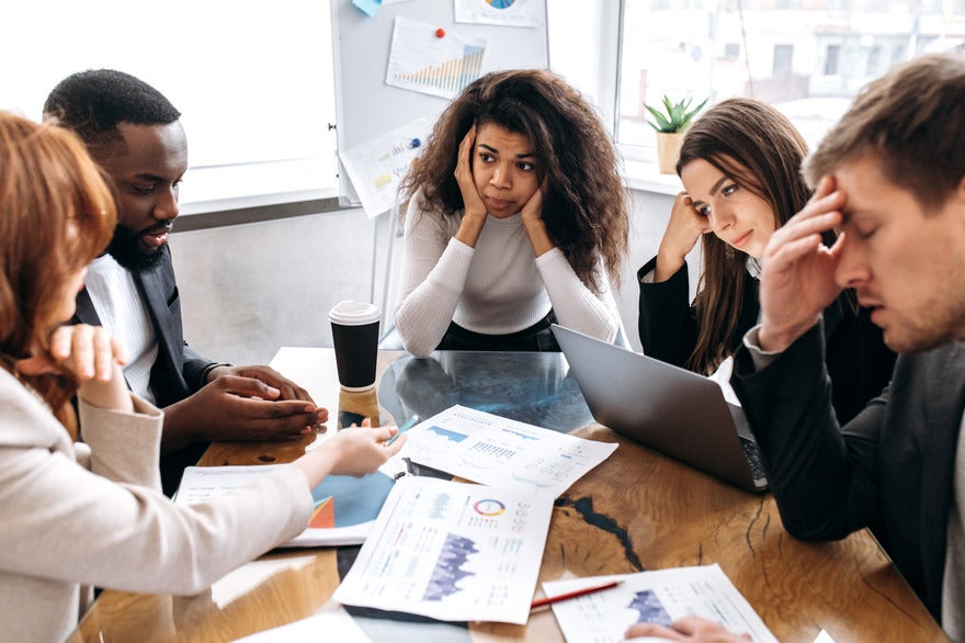 Group of people looking stressed around a work table as if trying to solve a problem