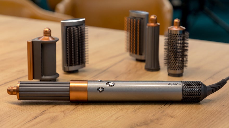 Orange and grey Dyson hairdryer with five attachment accessories placed behind it on a wooden table