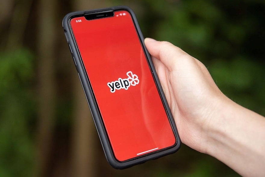 Hand holds a cellphone showing the Yelp logo