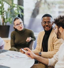 Group of office workers chatting around a table with laptops and paper in front of them